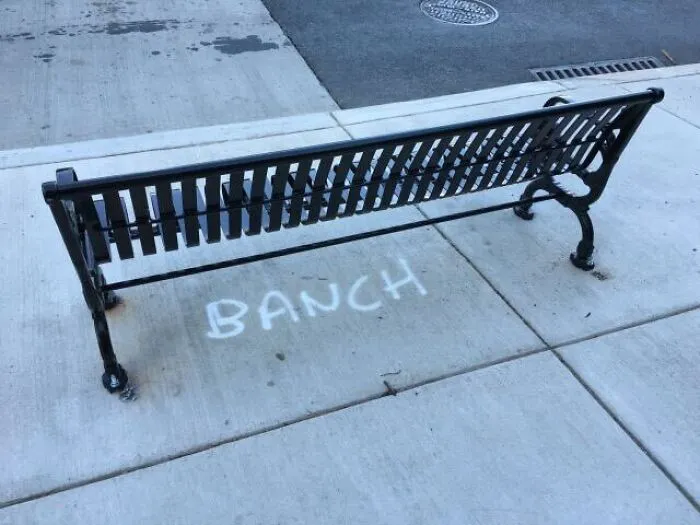 A park bench with the word BANCH spray painted on the sidewalk, a hilarious spelling fail