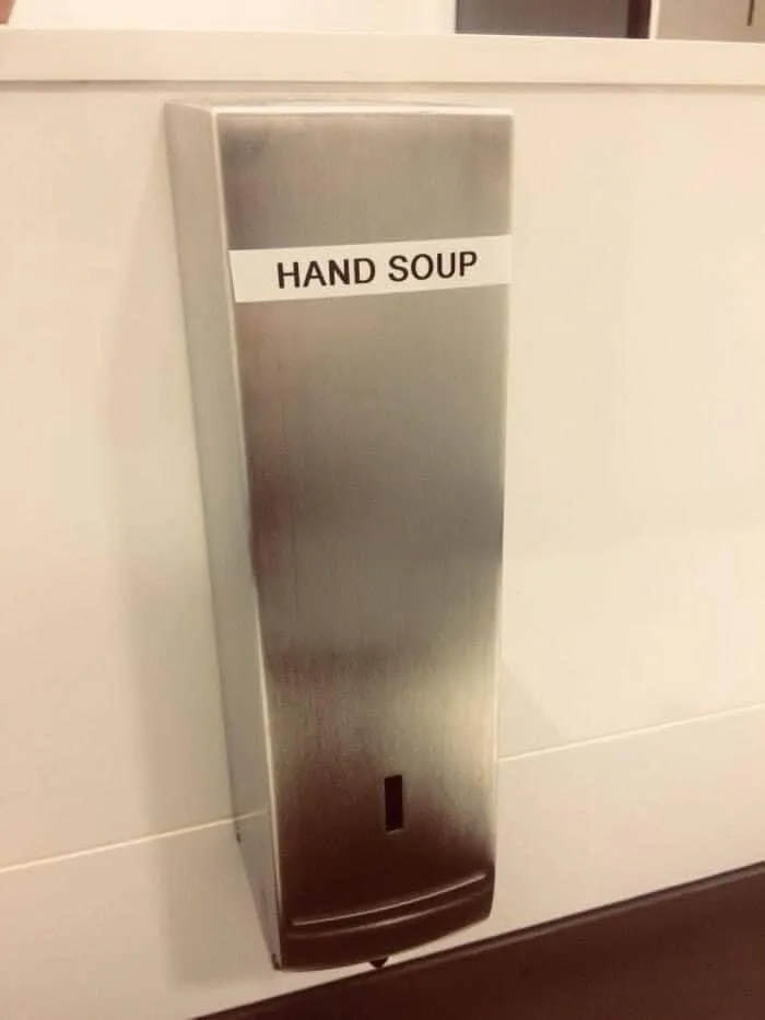 A metallic soap dispenser labeled HAND SOUP, showing funny spelling fails that change the meaning of words.