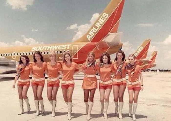 Flight attendants in orange uniforms posing in front of planes in old photos of America.