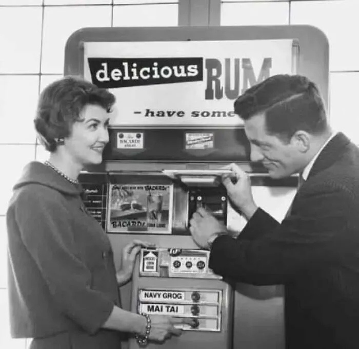 Man buying drinks from a vintage rum vending machine featured in old photos of America.