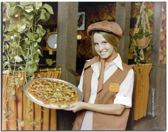 A 1970s waitress holding a freshly baked pizza, featured in old photos of America.