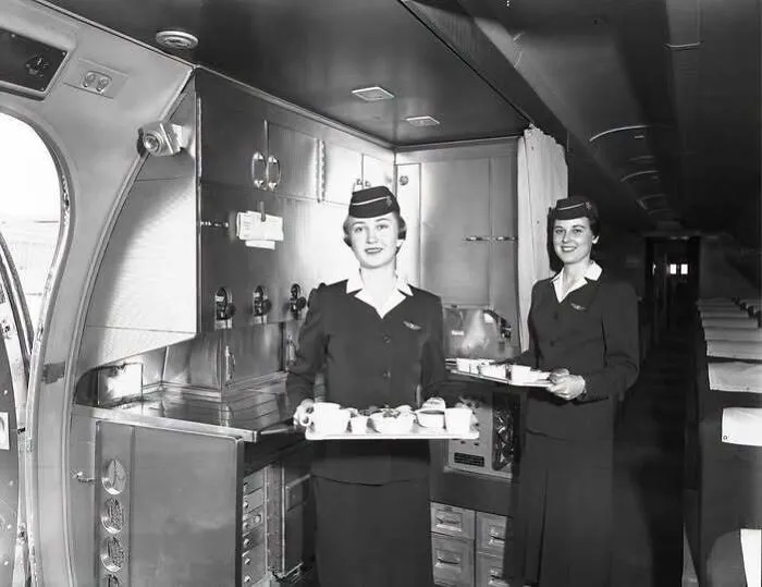 Black and white old photo of flight attendants preparing food in an airplane kitchen in America