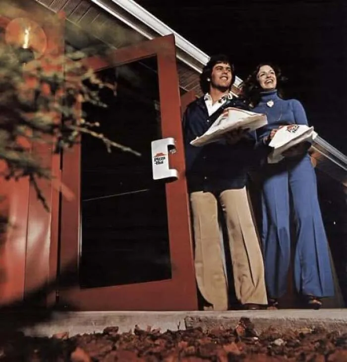 A happy young couple leaving a Pizza Hut restaurant in an old photo of America.