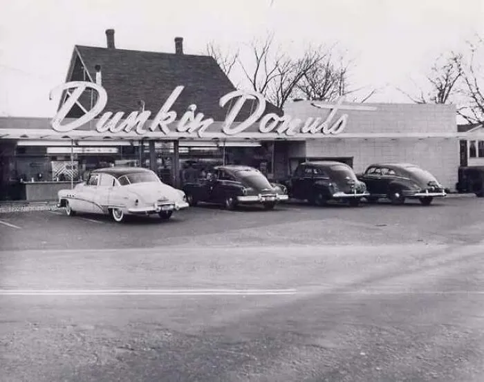 Black and white vintage picture showcasing classic cars parked outside an early Dunkin Donuts storefront