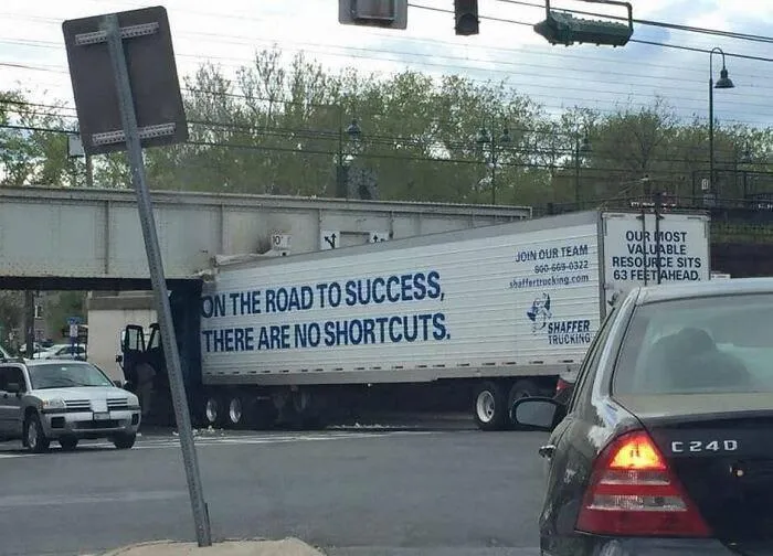 Commercial trailer stuck under a low bridge with a ironic slogan about no shortcuts