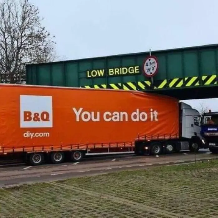 Large orange B and Q delivery truck stuck under a low bridge, creating a moving joke.