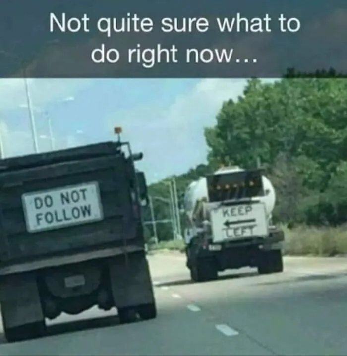 Two trucks on the highway displaying conflicting road instruction signs