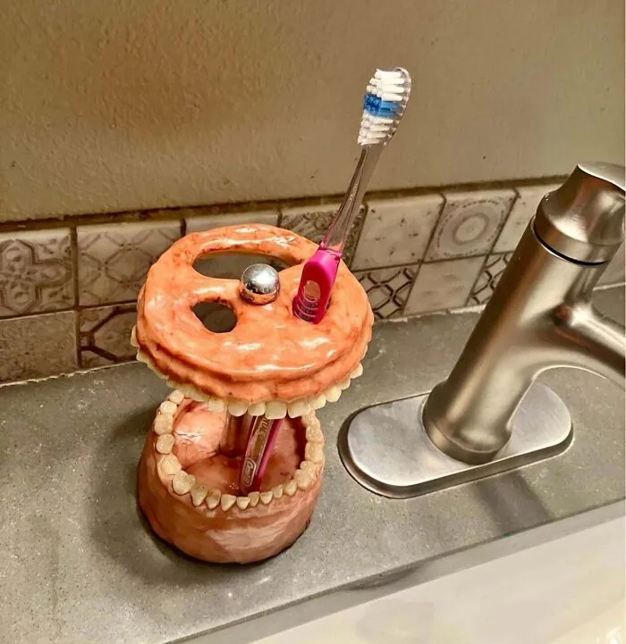 An awful toothbrush holder creation shaped like realistic gums and teeth next to a sink.