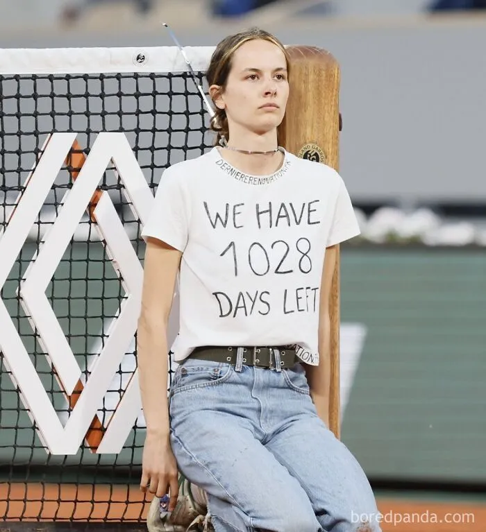 A protester kneeling at a tennis net wearing a t-shirt about climate time running out, a dark dystopian meme.