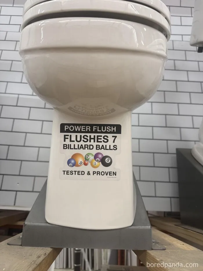 Toilet with a sticker claiming it flushes seven billiard balls, demonstrating odd measuring units.