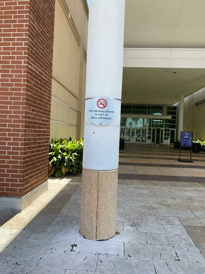 A perfectly confusing photo of a round pillar with a sign attached near a mall entrance.
