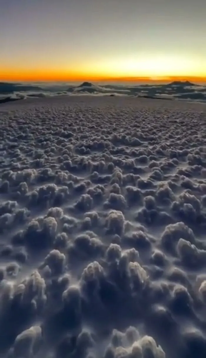 A perfectly confusing photo of sunset over a thick sea of clouds that looks like a textured landscape