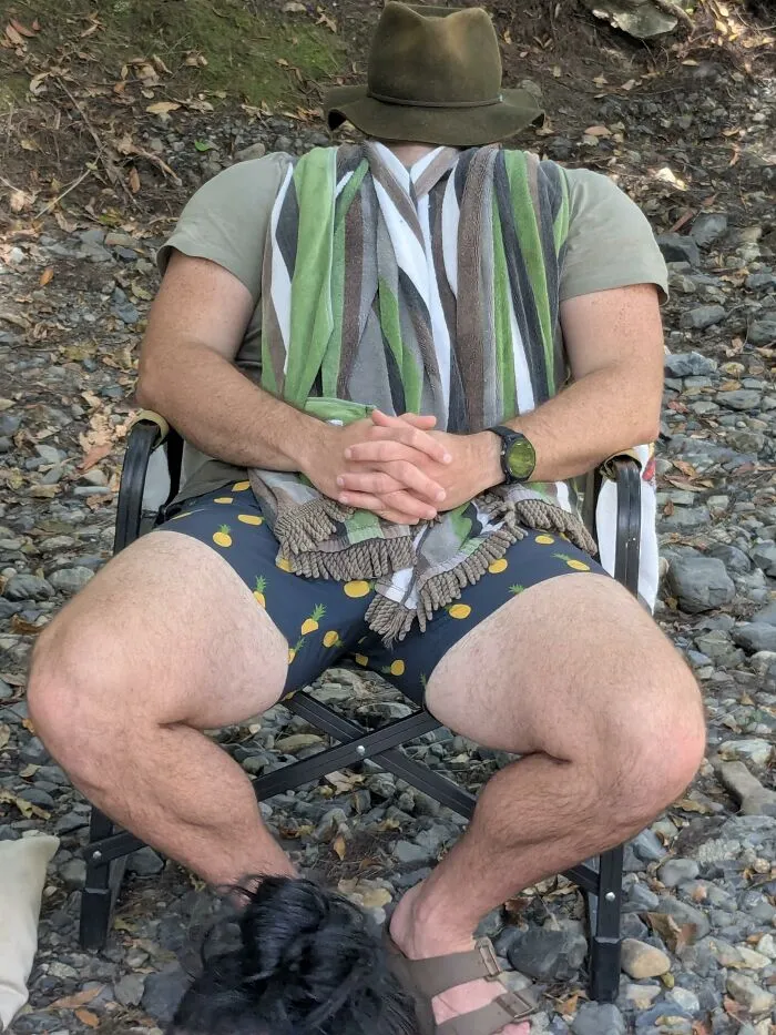 A perfectly confusing photo of a man in a hat sitting in a chair with his face completely obscured by his towel