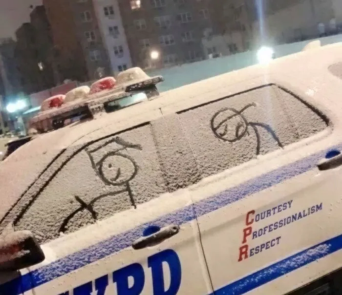 A stick figure driver drawn on a snow-covered police car, showing a lighthearted act of vandalism.