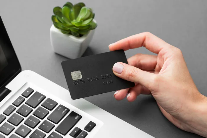 A hand holding a black credit card near a laptop, symbolizing financial disputes in divorce stories.