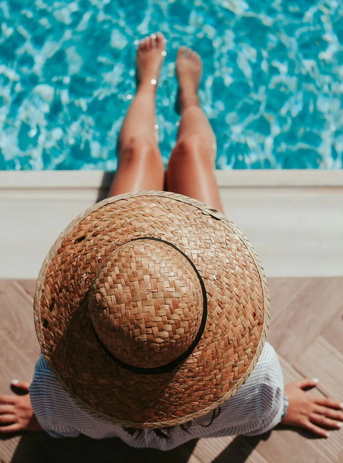 Woman relaxing by pool wearing straw hat representing bridezilla stories about destination events.