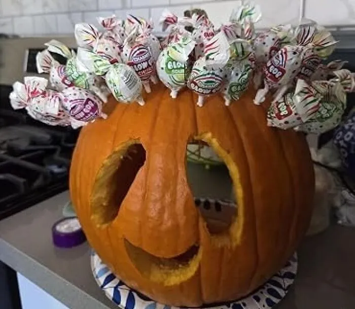 A carved Halloween pumpkin decorated with lollipops sticking out of the top, perfect for Halloween candies lovers