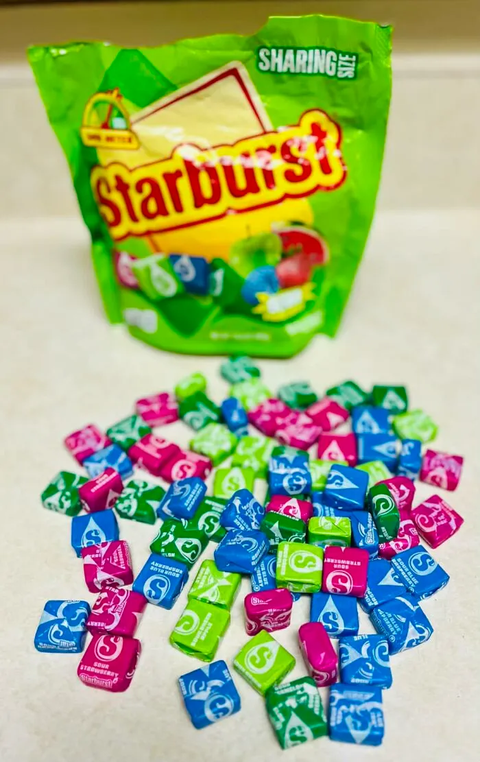 A pile of colorful chewy Starburst candies spilled in front of a green bag for Halloween candies lovers