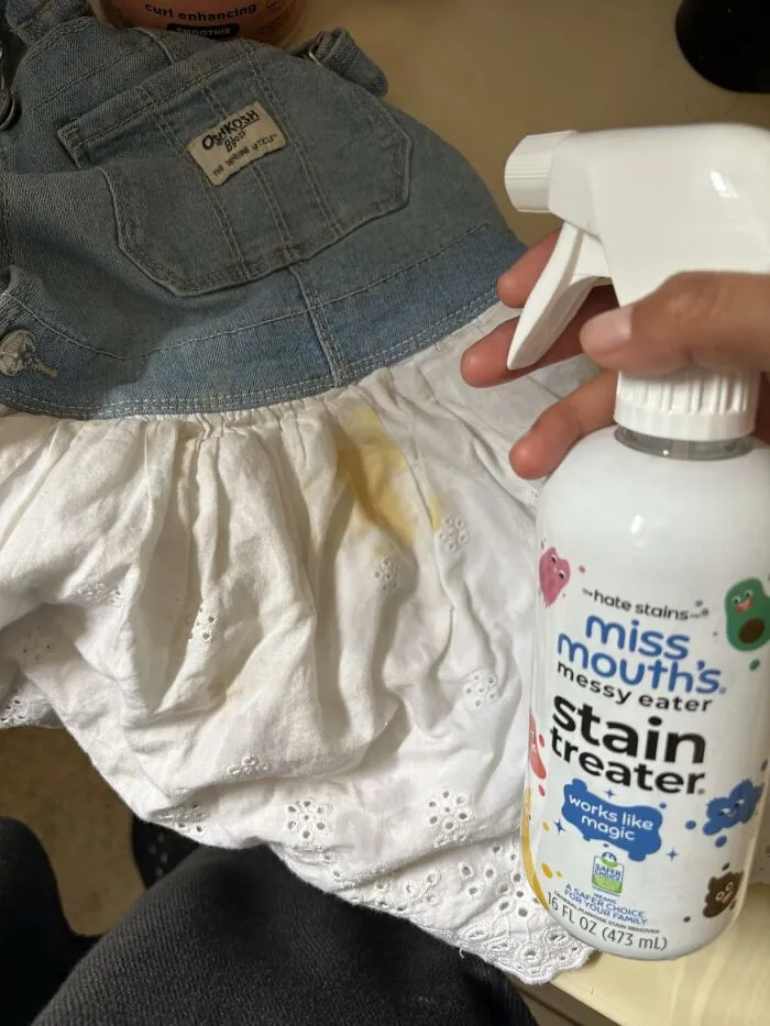 Spraying Miss Mouth's messy eater stain treater on a baby dress, an Amazon Big Deal Days trending item