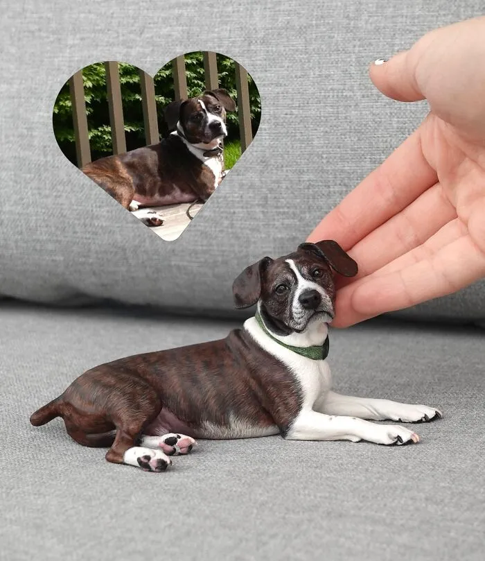 Handmade hyperrealistic sculpture of a lying brindle dog beside a reference photo.