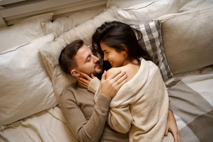 A loving couple lying together on a bed, reflecting back on past divorce stories.
