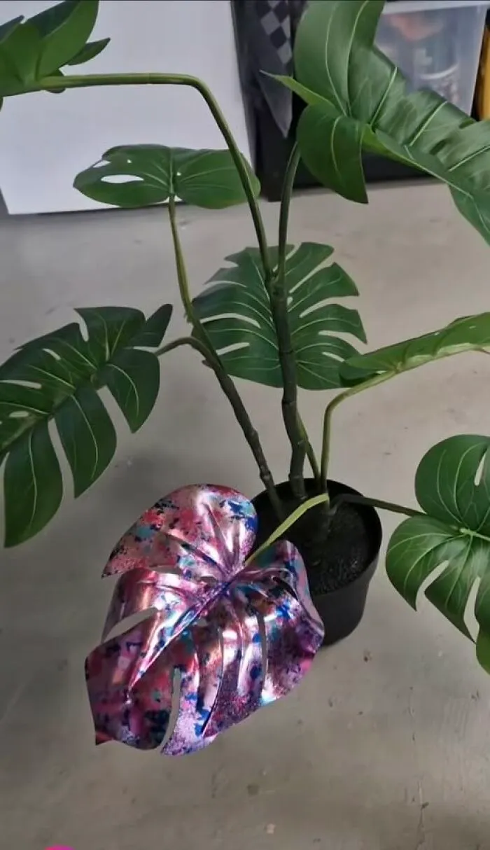 An artificial houseplant with one single leaf painted in metallic pink and blue, showcasing hilarious art projects.