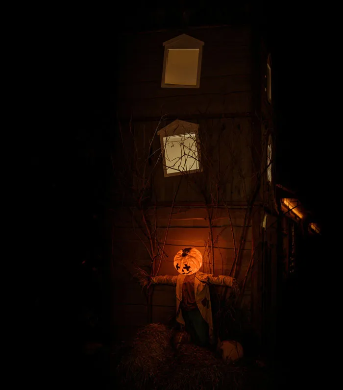 A eerie glowing pumpkin scarecrow standing outside a dark house for scary Halloween stories.