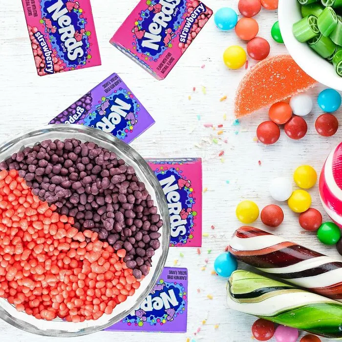 Colorful Nerds candy scattered near a glass bowl filled with red and purple Nerds for Best Halloween Candies.