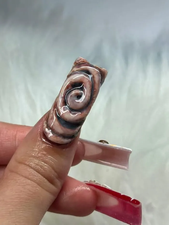 A strange art project featuring acrylic nail design made to look like a cinnamon roll.