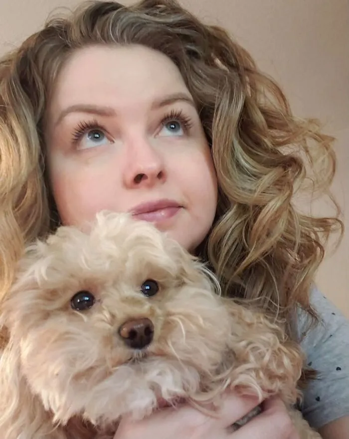 A woman with curly blonde hair and her fluffy dog looking up together, illustrating pets that look like their owners.