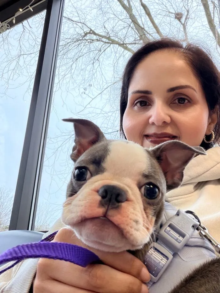 A smiling woman holding a cute puppy with a matching expression, showcasing pets that look like their owners.