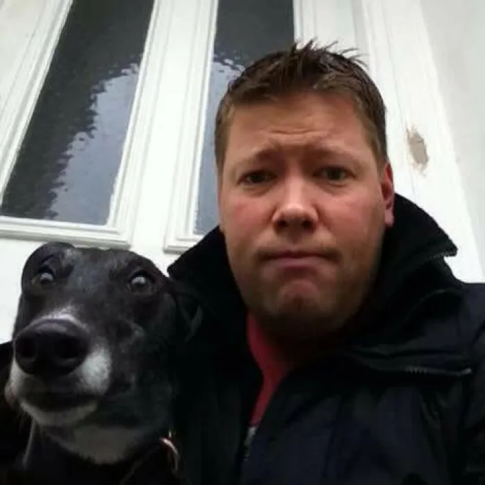 A man and his black greyhound making similar serious expressions, proving pets look like owners