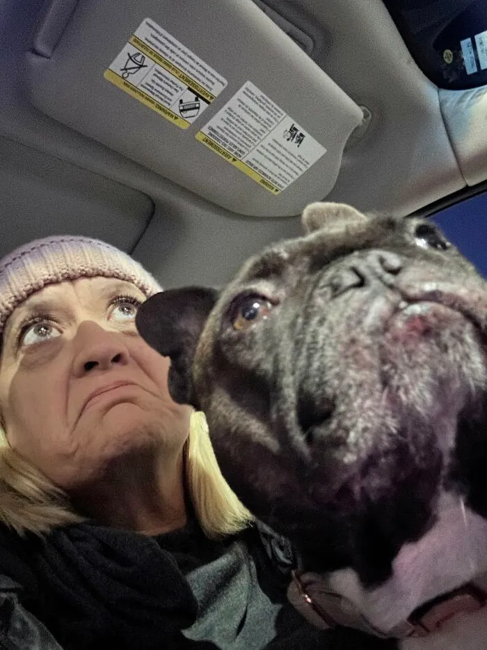 A woman and her dark French bulldog making the same funny face, showcasing pets that look like their owners