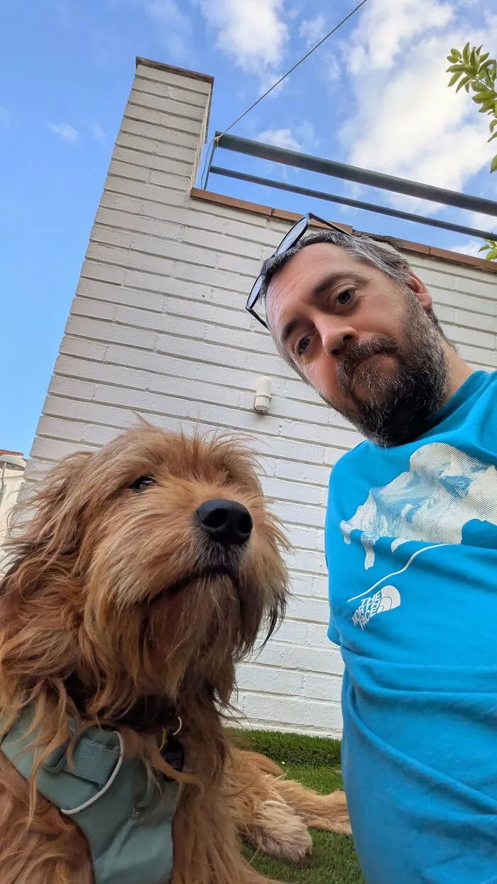 A bearded man in a blue shirt with his fluffy brown dog that looks like its owner