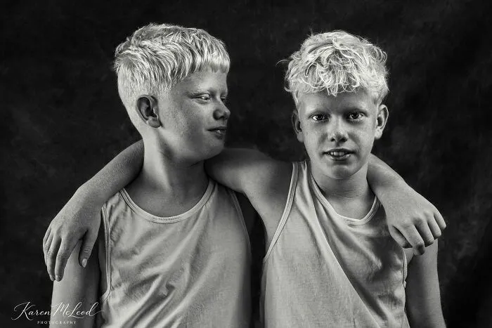 A black and white portrait photo of two young boys with light curly hair hugging each other