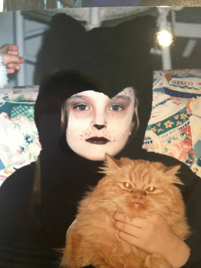 Funny family photos with cats showing a child dressed as a cat holding a fluffy orange cat