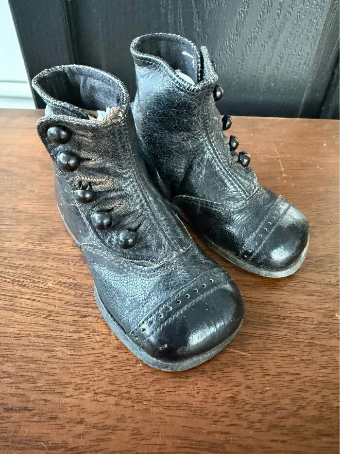 Pair of vintage black leather antique boots with button details on wooden surface thrift store find