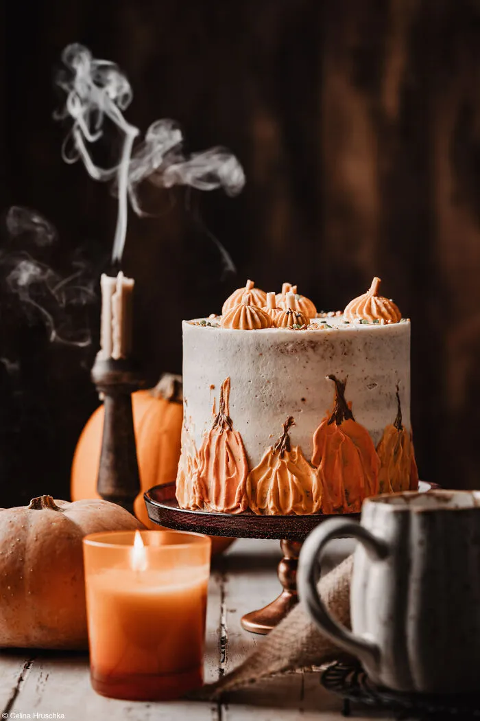 Decoared autumn cake with pumpkin icing art beside a smoking candle.