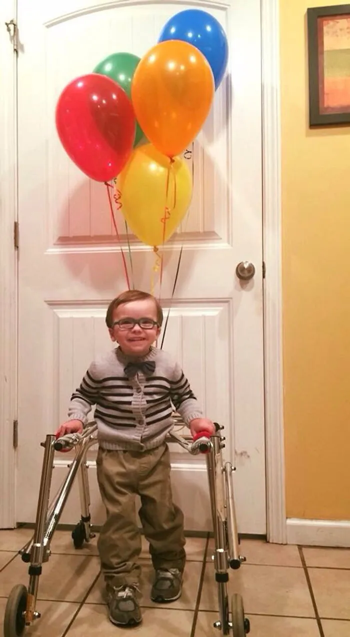 Young boy using a walker dressed up with colorful balloons attached to it.
