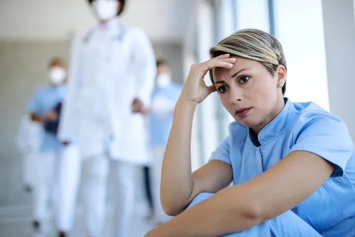 An exhausted healthcare worker sits in a hospital corridor, resting after a long, stressful shift