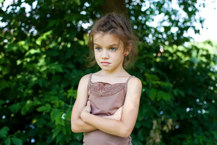 A disappointed young girl with arms crossed standing outside, showing infuriating feelings.
