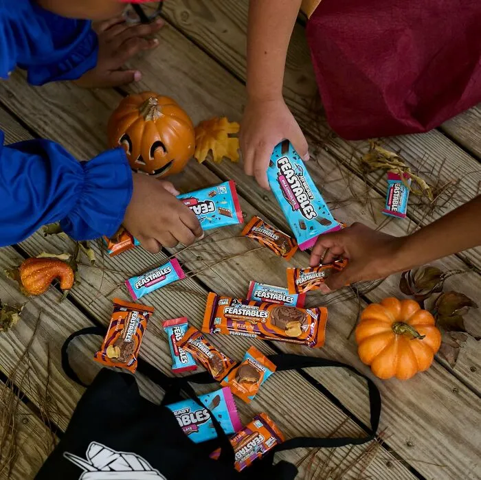 Hands reaching for Feastables chocolate bars surrounded by mini pumpkins for Best Halloween Candies.
