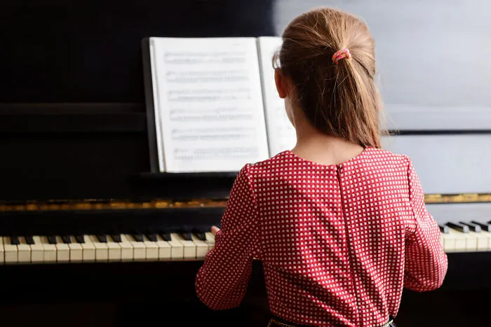 Young girl practicing piano under close supervision, symbolizing strict helicopter parenting.