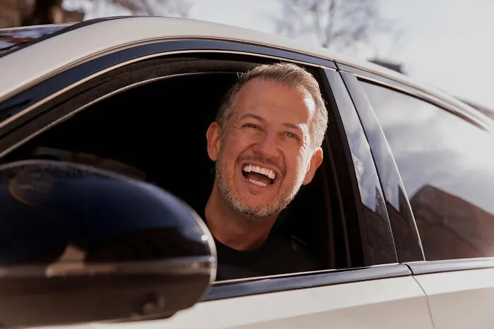 Man laughing happily out a car window, highlighting emotional outcomes in divorce stories.