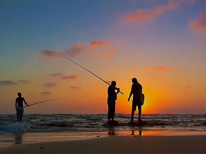 Silhouettes of people fishing at sunset on the beach captured by iPhone