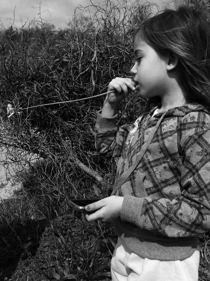 Black and white photo of girl holding flower and smartphone outdoor iPhone capture