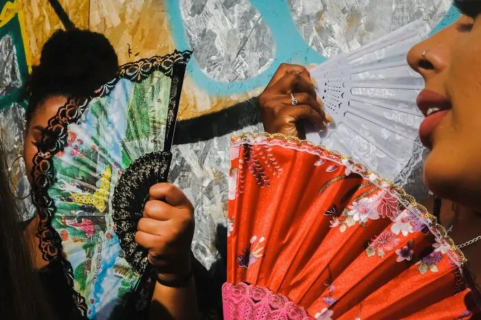 Two people holding decorative hand fans with vibrant colors in a sunny outdoor setting