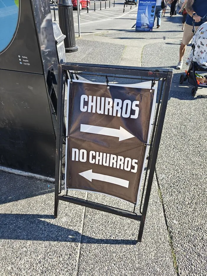 An A-frame sign pointing left and right with absurd signs for Churros and No Churros.