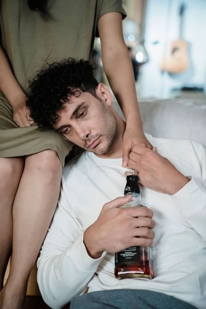 Sad man holding a bottle of alcohol leaning on a partner, depicting relationship strain that leads to choose divorce.