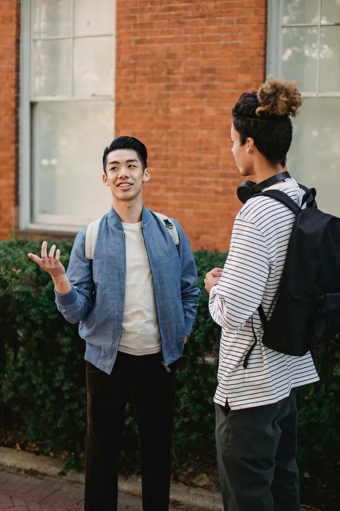 Two young men casually chatting outdoors against a brick wall